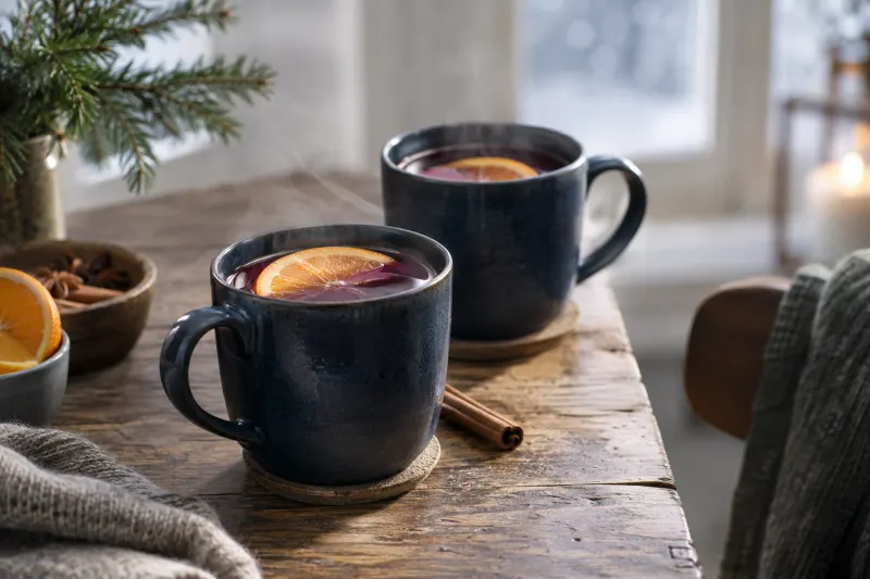 Warmer Fruchtpunsch mit Orangenscheibe und Zimt in schlichten Bechern